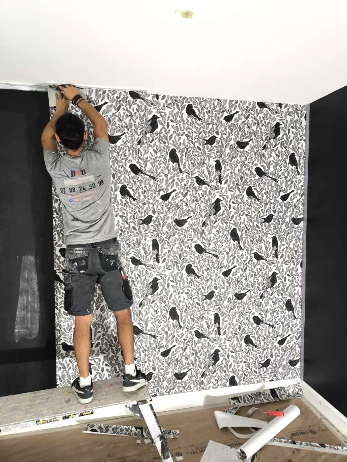 Ugur, en t-shirt DOD Peinture, pose un papier peint avec soin sur un chantier.